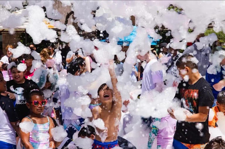 Large group of kids at a school foam event with a boy reaching up through the foam